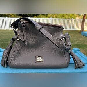 Dooney & Bourke pebbled leather tassel shoulder bag. Color is a grayish/tan.
